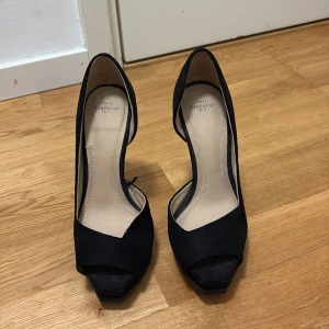 Svarta mocka pumps från Zara Trafaluc - Snygga svarta pumps i mocka från Zara Trafaluc med öppen tå och hög klack. Skorna har en stilren design med plattform framtill och rundad häl. Perfekta för dig som vill ha en klassisk men trendig look.