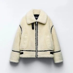 Beige teddyjacka från Zara - Säljer en beige teddyjacka från Zara med svarta detaljer och dragkedja framtill. Jackan har stor krage, markerade sömmar och två fickor på sidorna. Perfekt för kalla dagar och ger en cool, avslappnad vibe.