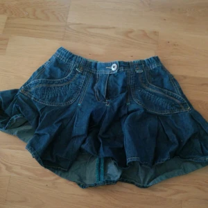 Blå jeanskjol - Snygg blå jeanskjol från Myshirt i kort modell med coola fickdetaljer fram och bak. Kjolen har markerade sömmar och veckad nederdel som ger extra volym. Perfekt för dig som gillar en avslappnad och trendig stil. Står storlek 158 men skulle gissa att den passar som XS i vuxenstorlek💞