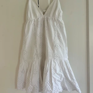 Klänning från Zara - Superfin vit kortklänning från Zara med broderade blommor och spetsdetaljer. Klänningen har smala axelband, knytning i ryggen och volang nertill. Perfekt för varma dagar och har en luftig passform i bomull. Såg nu att de finns en liten fläck på framsidan, men skulle slå vad om att den går bort i tvätten!! 🌟🌟
