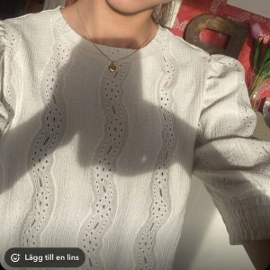 Vit blus med puffärm från Pieces - Supersöt vit blus från Pieces med korta puffärmar och vågformade broderade detaljer. Blusen har rund halsringning och är i ett lätt, luftigt tyg som känns perfekt för vår och sommar. Snygg struktur och romantisk känsla!