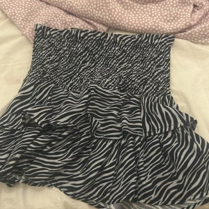 Zebramönstrad kort klänning Gina Tricot - Supersnygg kort klänning från Gina Tricot med svartvitt zebramönster. Klänningen är axelbandslös med smock upptill och volangig kjol. Perfekt för dig som vill sticka ut med ett djurmönster och gillar trendiga detaljer.