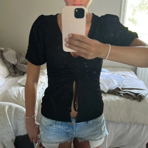 Svart topp med snörning och puffärm - Snygg svart topp med v-ringning, puffiga korta ärmar och trendig snörning framtill som ger en cool rynkad effekt!💗💗
