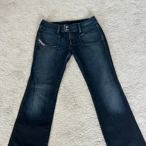 Mörkblå Diesel jeans bootcut - Snygga mörkblå jeans från Diesel med bootcut passform. Jeansen har två knappar i midjan, stora framfickor och klassisk Diesel Industry-logga på fickan. Materialet är jeans med lätt slitning för en cool look. Använda fåtal gånger. Midjemått: 43, Innerbenslängd: 77. Dom är liiite långa på mig som är 156 cm! (Reser bort den 22 juli i 3 veckor, så köp gärna innan dess)🩵😊