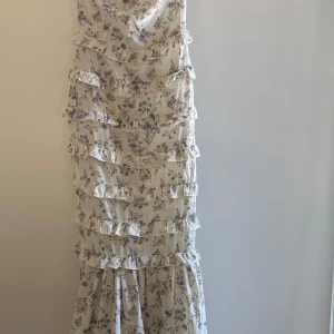 Blommig långklänning  - Helt ny med lappenkvar supersöt långklänning från Boohoo i ljusbeige med blommigt mönster i lila och brunt. Klänningen har flera lager volanger. Perfekt för sommarens alla tillfällen. Materialet är lätt och luftigt, vilket gör att den inte är för varm! 