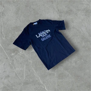 Svart Lanvin Galerie t-shirt - Snygg svart t-shirt från Lanvin Galerie med tryck framtill och en stor grafisk logga på ryggen. Klassisk passform med korta ärmar och rund hals. Perfekt för dig som gillar streetstyle och vill sticka ut med ett exklusivt märke.