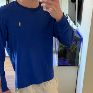 Blå långärmad tröja i bomull - Tröja är inte smutsig, det är en spegel.En enkel och stilren blå långärmad tröja i mjuk bomull. Tröjan har en klassisk passform och rund halsringning, perfekt att matcha med jeans eller chinos för en clean look.