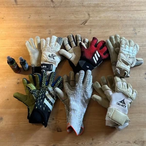Flera par målvaktshandskar Adidas, Select - Säljer ett gäng målvaktshandskar från Adidas, Select. Färgerna är blandade: svart, vit, röd, grön och grå. Några har coola mönster och detaljer, vissa med klassiska ränder. Perfekta för fotbollsträning eller match!