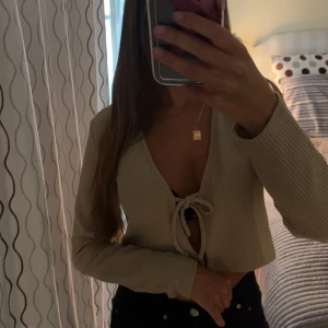 Beige croppad ribbad bolerotopp - Trendig beige croppad bolerotopp med långa ärmar och snygg knytning framtill. Toppen är ribbad och har en djup v-ringning som ger en cool och avslappnad vibe. Perfekt att styla över ett linne eller topp för en modern look. Passar mig som vanligtvis är en XS likaså en person som använder M beroende på vad för passform man vill ha💕