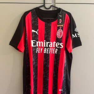 AC Milan Puma fotbollströja röd/svart - AC Milan matchtröja från Puma i rött och svart med klassiska vertikala ränder och subtilt mönster i det svarta. Tröjan har klubbmärke och Puma-logga på bröstet samt sponsortryck. Tillverkad i lätt och ventilerande polyester, perfekt för fotbollsplanen.