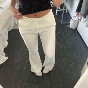 Vita kostymbyxor med bootcut - Snygga vita kostymbyxor med bootcut. Byxorna har raka ben som blir vidare nertill, diskreta fickor och stängs med dragkedja och knapp. Perfekta för en clean och stilren look. Materialet känns mjukt och har en lätt stretch.