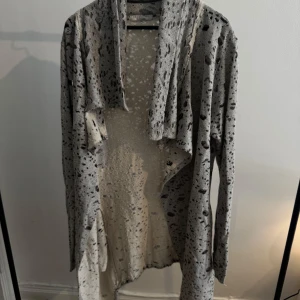 Gråmönstrad kofta från Xagon Man - Säljer en lång, grå kofta från Xagon Man med svartprickigt mönster. Koftan har en öppen front med draperad krage och långa ärmar. Materialet är mjukt och stretchigt, perfekt för lager-på-lager. Snygg till både jeans och t-shirt. Nypris 2000:-