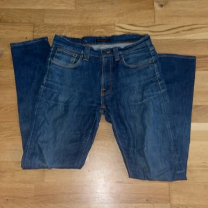 Nudie jeans - Säljer ett par klassiska blå jeans från Nudie Jeans med snygga kontrastsömmar och ikonisk broderad bakficka. Modellen heter lean dean Perfekta för dig som gillar stilrena och tidlösa jeans. De är lagade på på backfickan vilket ja inte tycker syns. Storlek 32/34. 