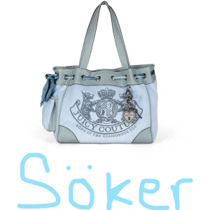 SÖKER Juicy Couture Daydreamer väska blå - Stor Daydreamer handväska från Juicy Couture i ljusblått och grått med dubbla handtag, snörning upptill och dekorativt emblem framtill. Väskan har en söt rosett på sidan och ett hängande hjärtsmycke. Insidan är fodrad med Juicy Couture-tryck.