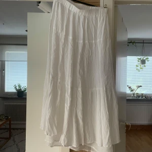 Vit långkjol i bomull - Luftig och flowy vit långkjol med lätt rynkad struktur och resår i midjan. Perfekt för varma dagar och enkel att styla med crop tops eller stickade tröjor. Kjolen har en mjuk och skön känsla tack vare bomullsmaterialet.  Ca 80cm lång.