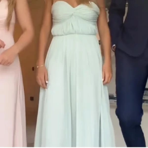 Balklänning  - Superfin mintgrön balklänning med axelbandslös design och twistad drapering över bysten. Klänningen har ett flowy fall och är perfekt för bal eller student. Materialet känns lätt och luftigt, vilket ger en elegant look. 