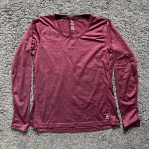 Vinröd långärmad träningströja SOC - Vinröd långärmad träningströja från SOC med rund halsringning och diskret reflexdetalj på ryggen. Tillverkad i ett lätt och stretchigt syntetmaterial som andas, perfekt för löpning eller gym. Snygg passform och enkel design som funkar till all träning.