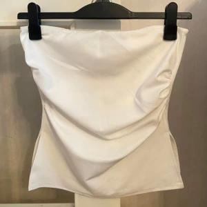 Vit  tubtopp med slits - Säljer en stilren vit  tubtopp med slits på sidan. Toppen är axelbandslös och har en clean, enkel look som passar perfekt till sommarens outfits. Materialet känns mjukt mot huden.