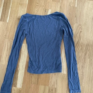 Blå långärmad topp från Gina Tricot - En basic blå långärmad topp från Gina Tricot i storlek XS. Toppen har en djup v-ringning och är gjord i mjuk bomull, perfekt att styla med jeans eller kjol. Enkel och stilren design som funkar året runt.