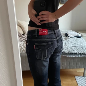 M.K. Jeans mörkblå bootcut jeans - Mörkblå bootcut jeans från M.K. Jeans med snygga slitningar och kontrastsömmar. Klassisk femficksmodell med markerade bakfickor och röd logotyppatch i midjan. Jeansen har låg midja och är tillverkade i slitstarkt denimtyg.