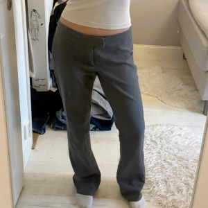 Lågmidjade Bootcut Kostymbyxor  - Mörkgrå Lågmidjade Kostymbyxor från Nelly i en bootcut passform. Byxorna har en unik gylf-design och inga fickor. Byxorna ger en superfin hudnära form och är lite stora på mig som vanligtvis har storlek 34-36 men sitter fortfarande supersnyggt! jag skulle säga att dom passar alla från 160-175cm. köpta för 400kr men säljer väldigt prisvärt då det saknas 1 av 3 knappar (inget som märks av!) och att de är lite slitna vid fötterna. önskas bild på detta kontakta mig!🩷