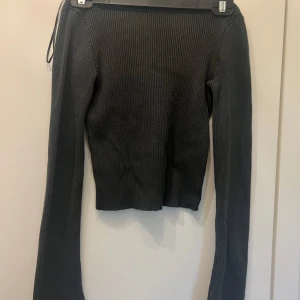 Svart ribbad croppad tröja - Säljer en svart, ribbstickad tröja med croppad passform och långa ärmar. Tröjan har en bred, rundad urringning både fram och bak vilket ger en snygg och trendig look. Perfekt att styla med jeans eller kjol för en chill vibe.