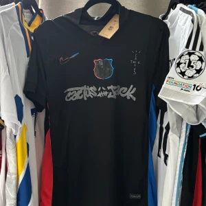 Svart FC Barcelona x Nike Cactus Jack tröja - Unik svart FC Barcelona fotbollströja från Nike med trycket 'Raphinha 11' på ryggen. Tröjan har coola detaljer som klubbmärke och Nike-logga i svart med röd och blå kant, samt grafitti-inspirerat tryck på bröstet. Tillverkad i lätt och ventilerande material. (Den dåliga reviewen beror på att jag hade glömt bort lösenordet, men denna gång lovar jag att skicka iväg tröjan när den köps) :)