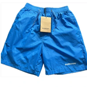 Badshorts från Burberry - Säljer ett par snygga och stilrena badshorts från Burberry . Diskret BURBERRY-logga framtill och klassisk design. Perfekta för sommaren eller semestern!  ✔️ Storlek: M ✔️ Färg: Blå ✔️ Skick: Helt nya –  tag kvar ✔️ Passform: Normal   Nypris ligger runt 3000 kr – passa på att fynda till bättre pris! Skicka gärna ett meddelande vid frågor 😊