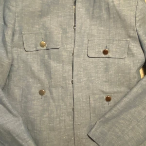 Ljusblå kavaj från Zara - Snygg ljusblå kavaj från Zara med fyra stora fickor framtill och silvriga knappar. Kavajen har en klassisk rak passform och är tillverkad i ett linneliknande material som ger en fräsch och stilren look. Perfekt för dig som vill ha en clean och modern vibe. Kom privat för fler frågor 💕