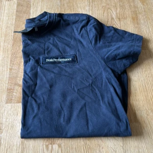 Svart Peak Performance t-shirt - Snygg svart t-shirt från Peak Performance med klassisk logga broderad på bröstet. T-shirten har rund hals och korta ärmar, perfekt för en clean och sportig stil. Tillverkad i mjuk bomull som känns skön mot huden.stryks innan köp
