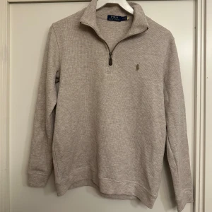 Beige half zip tröja från Polo Ralph Lauren - Säljer en beige långärmad tröja från Polo Ralph Lauren med half zip och klassisk krage. Tröjan har broderad logga på bröstet och är tillverkad i mjuk bomull. Perfekt för dig som gillar stilrena och tidlösa plagg med snygga detaljer.