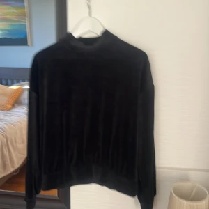 Svart sammetströja med polokrage - Säljer en svart långärmad tröja i mjuk sammet med polokrage. Tröjan har en loose passform och breda muddar vid ärmslut och nederkant. Perfekt för dig som gillar stilren och bekväm look.