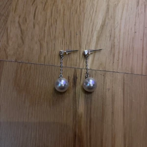Silvriga örhängen med pärla - Snygga örhängen med hängande design i silverfärgad metall och en rund vit pärla längst ner. Kedjan ger ett elegant intryck och pärlan reflekterar ljuset superfint. Perfekt för dig som gillar stilrena smycken med lite extra glans.