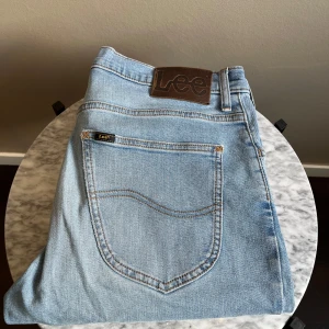 Lee Brooklyn ljusblå jeans W34 L36 - Snygga ljusblå jeans från Lee, modell Brooklyn. Klassisk femficksdesign med Lee-logga på bakfickan och läderpatch i midjan. Jeansen har raka ben och är tillverkade i bomull med kontrastsömmar. Perfekta för en avslappnad och stilren look.
