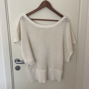 Vit stickad tröja med kort ärm - Säljer en vit stickad tröja med bred ribbad kant nedtill och vid ärmslut. Tröjan har en luftig meshstickad design och en bred, rund halsringning. Perfekt för lager-på-lager och chill stil.