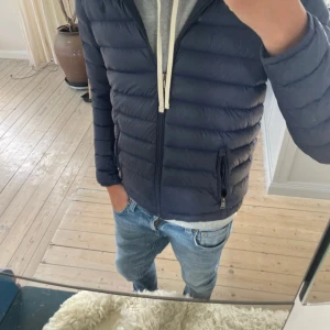 Mörkblå dunjacka från Ralph Lauren - Säljer en mörkblå dunjacka från Ralph Lauren med huva och dragkedja. Jackan är quiltad och har två fickor med dragkedja på sidorna. Perfekt för kyliga dagar och riktigt snygg till jeans eller hoodie. Det är en liten defekt på ryggen men ingen som syns vid användning 