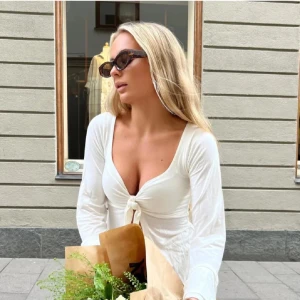 Vit topp med knytning från Design by Si - Supersöt långärmad vit topp med knytning från Design by Si som kan användas både till vardags eller fest. Säljer då den inte kommit till användning, är i gott skick. 💕☺️