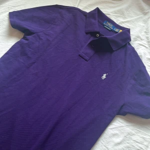 Lila Polo Ralph Lauren t-shirt - Snygg lila t-shirt från Polo Ralph Lauren med klassisk pikékrage och korta ärmar. Custom slim fit-modell med broderad logga på bröstet. Helt ny!!!