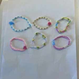 Färgglada pärlarmband med smileys - Sex handgjorda armband med pärlor i olika färger, vissa med smiley-ansikten och andra med stjärnor eller fiskar som detaljer. Perfekt för dig som gillar lekfulla och unika accessoarer. Armbanden är elastiska och passar de flesta handleder. 5kr styck! Om du köper alla 25kr!❤️