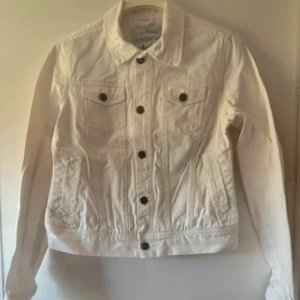 Vit jeansjacka från Havana - Snygg vit jeansjacka från Havana med klassisk krage, svarta knappar och två bröstfickor med lock. Jackan har lång ärm och raka linjer som ger en clean look. Perfekt att slänga över en t-shirt för en chill stil. Sparsam används. Storlek 34 men upplevs som 36.