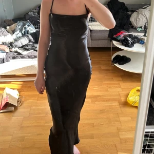 Svart satinklänning med slits - Svart satinklänning från ASOS. Storlek 36/S. Har en slits vid ena benet. Knytning i ryggen. Använd 1 gång. Jättefint och skönt material.