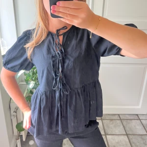 Svart blus med knyt och volang - Säljer min svarta blus med korta puffärmar och snygg knytning framtill. 