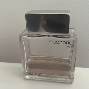 Calvin Klein Euphoria Men parfym - Snygg herrparfym från Calvin Klein, Euphoria Men. Flaskan är rektangulär i transparent glas med en stilren, silvrig fyrkantig kork. Vätskan har en svagt beige ton. Perfekt för dig som gillar klassisk och modern design.