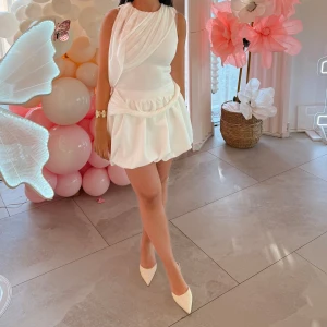 Vit kort omlottklänning med drapering - Supersnygg vit kort klänning med omlottdetaljer och draperad överdel. Kjolen har en ballongformad siluett och midjan är markerad. Använda endast 1 gång! 