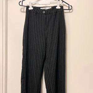 Svarta kostymbyxor med ränder Bershka - Snygga svarta kostymbyxor från Bershka med vita vertikala ränder. Byxorna har hög midja, raka ben och klassisk knappstängning fram. Perfekt för dig som gillar en stilren och trendig look. Passar till både sneakers och boots.