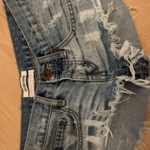 Blå jeansshorts från One Teaspoon - Snygga blå jeansshorts från One Teaspoon med slitna detaljer och fransig kant. Modellen är lågmidjad och har klassiska fem fickor, knapp och dragkedja framtill. Perfekt för sommarens alla äventyr, riktigt cool vintagekänsla. Köpte för 1299kr