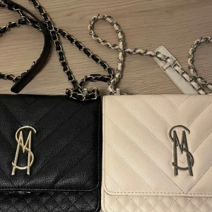 Steve Madden quiltad axelväska svart/beige - Säljer två snygga axelväskor från Steve Madden, en i svart och en i beige. Båda har quiltad design, kedjerem med läderdetaljer och metall-logga framtill. Perfekt storlek för mobilen och det viktigaste. Stilren look med lyxig känsla.