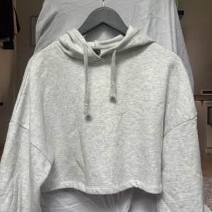 Ljusgrå croppad hoodie från Gina Tricot - Säljer en ljusgrå croppad hoodie från Gina Tricot i storlek XS. Tröjan har huva med snörning och är tillverkad i bomull. Jag vet inte om det är en fläck eller det är i meleringen (se bild 4) Kontakta om du har funderingar !!❤️