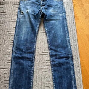 Dsquared2 blå jeans storlek 54 - Snygga blå jeans från Dsquared2 i storlek 54. Modellen har låg midja och normal passform med slitningar och coola detaljer på framsidan. Klassisk femficksdesign och tydliga Dsquared2-loggor på insidan och bak. Perfekta för dig som gillar street och premiumkänsla.