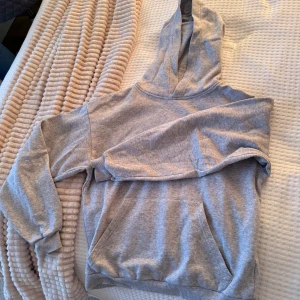 Grå hoodie med huva och ficka - Säljer en enkel och chill grå hoodie med stor huva och magficka. Perfekt för att slappa hemma eller dra på sig till skolan. Mjuk bomullskänsla och ribbade muddar vid ärmar och nederkant. Passar dig som gillar basic och comfy stil.